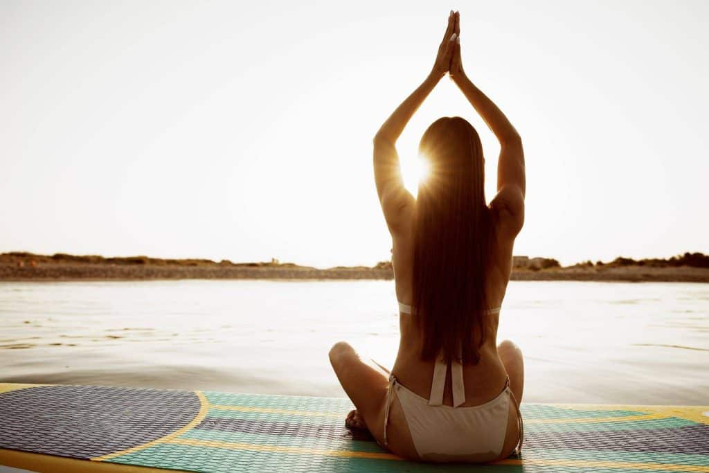 Young Woman practicing yoga on the paddle board in the morning on a yacht charter vacation
